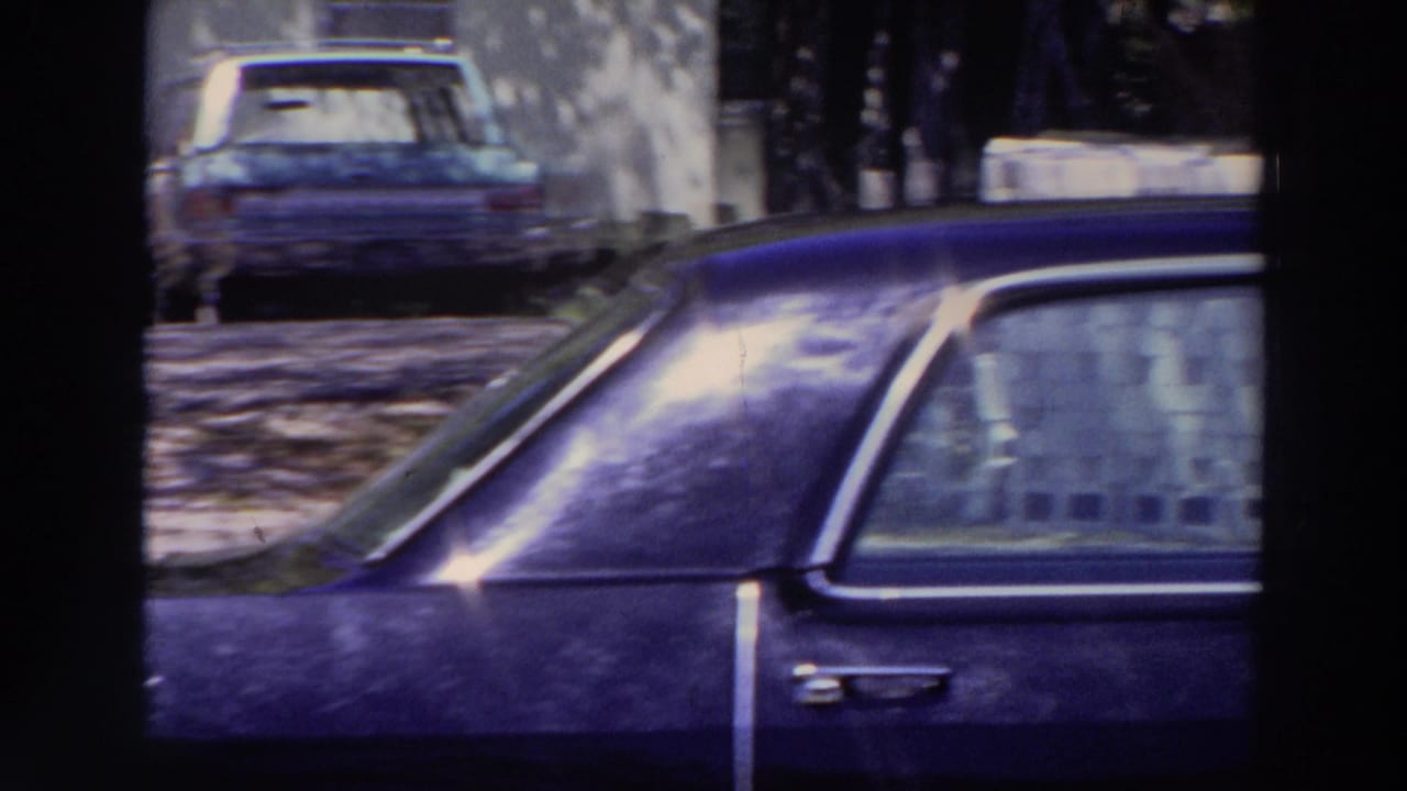 1966 Puerto Rico 8mm frame showing a dark parked sedan on a quiet street, with a person in light clothing visible in the background.