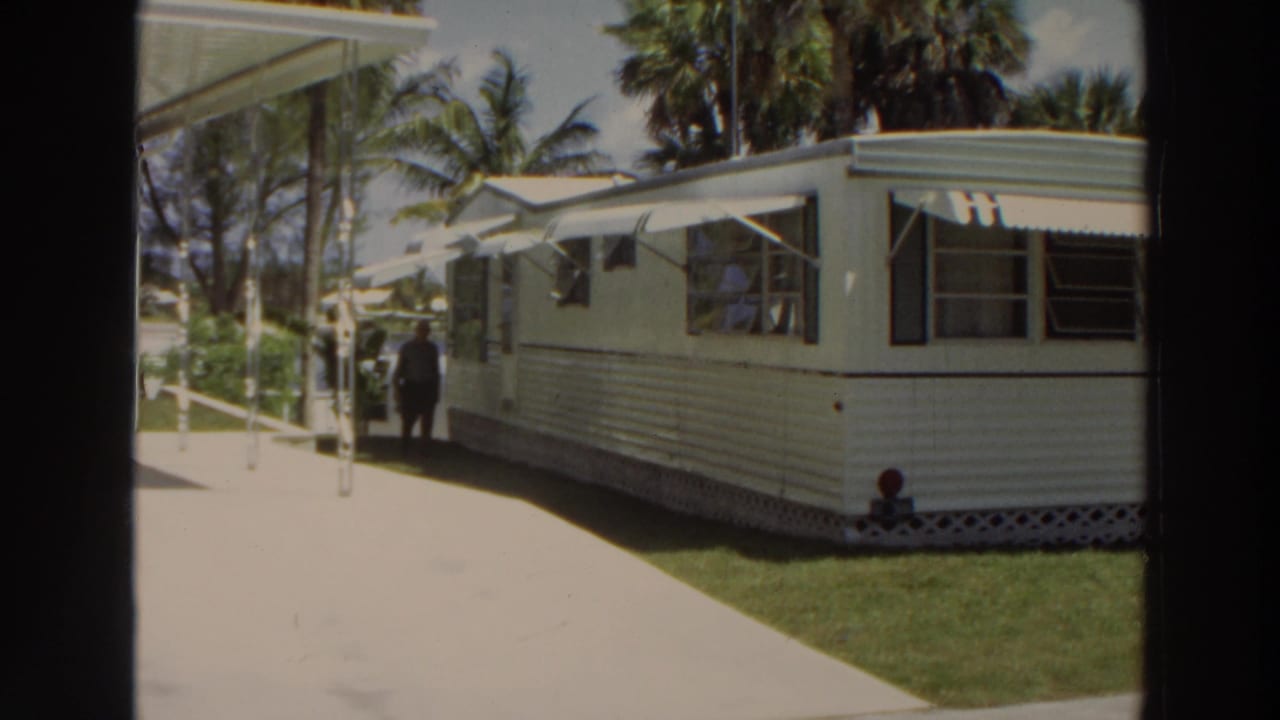 Man in dark clothing stands or walks near the mobile home side path.
