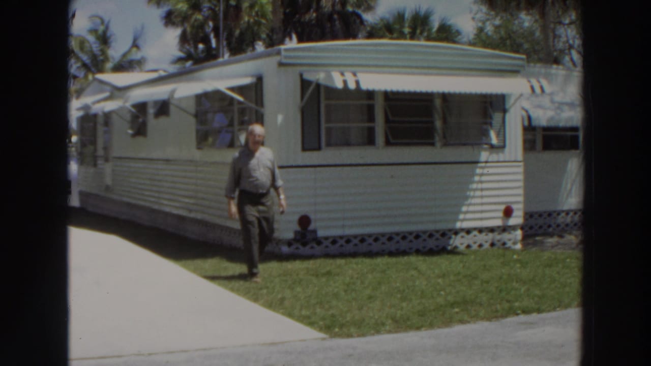 A closer 1966 Puerto Rico frame shows the man on the grass beside the white mobile home, with driveway and awning windows behind him.