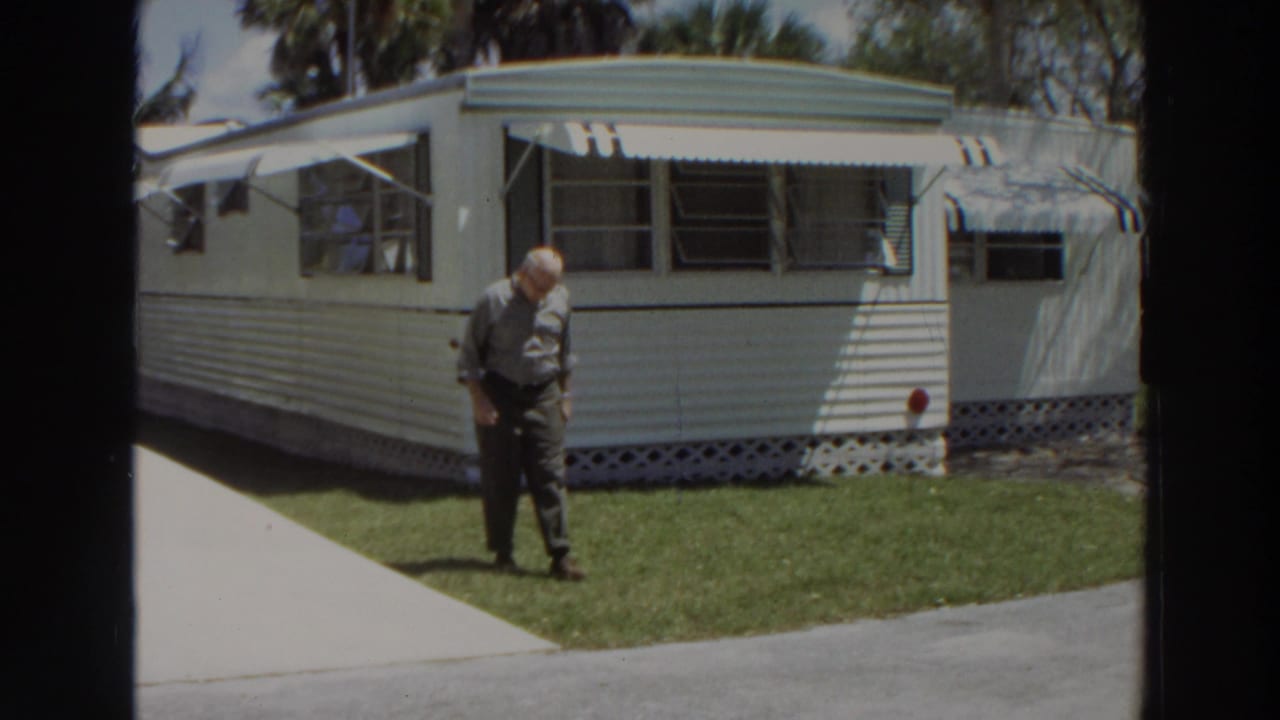 Near the end of the clip, the man looks down while crossing the lawn in front of the Puerto Rico mobile home exterior.