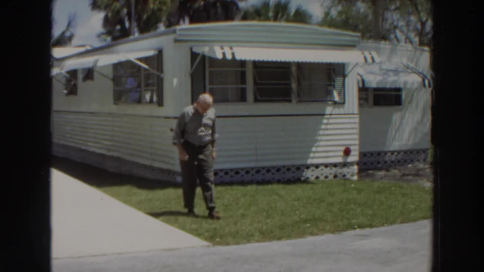 Near the end of the clip, the man looks down while crossing the lawn in front of the Puerto Rico mobile home exterior.