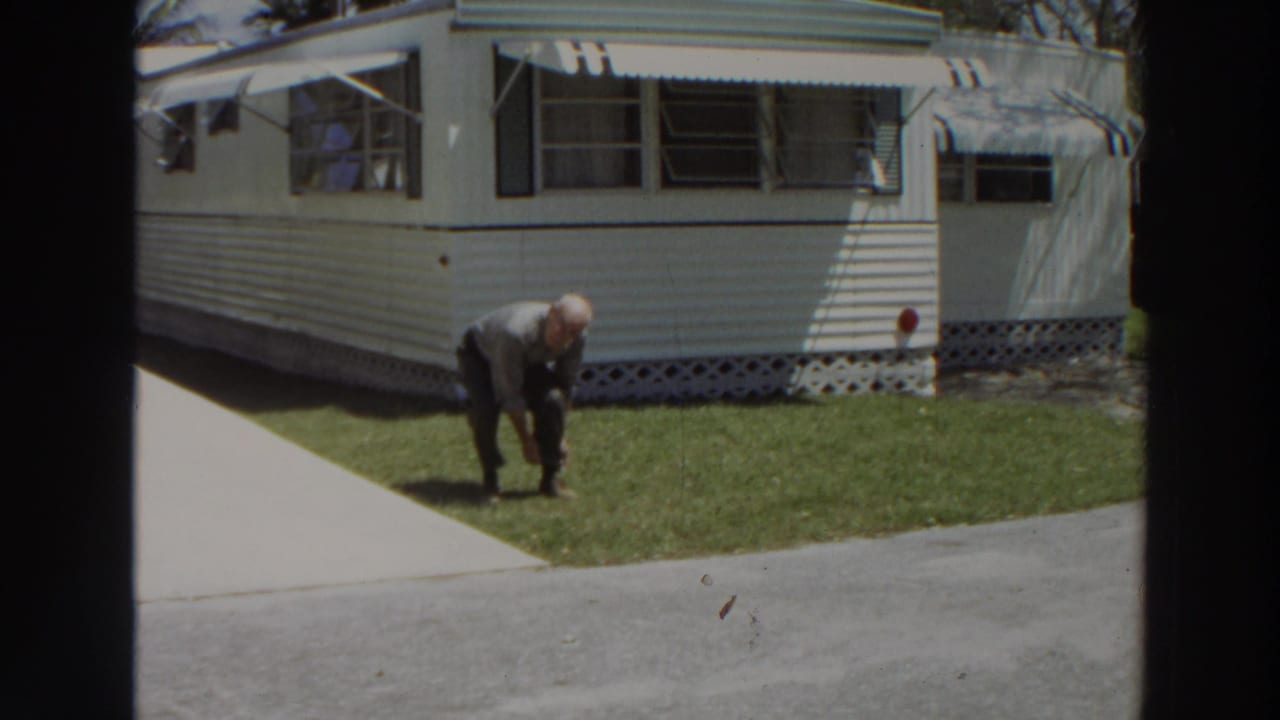 Man standing partly bent on grass in front of a mobile home.