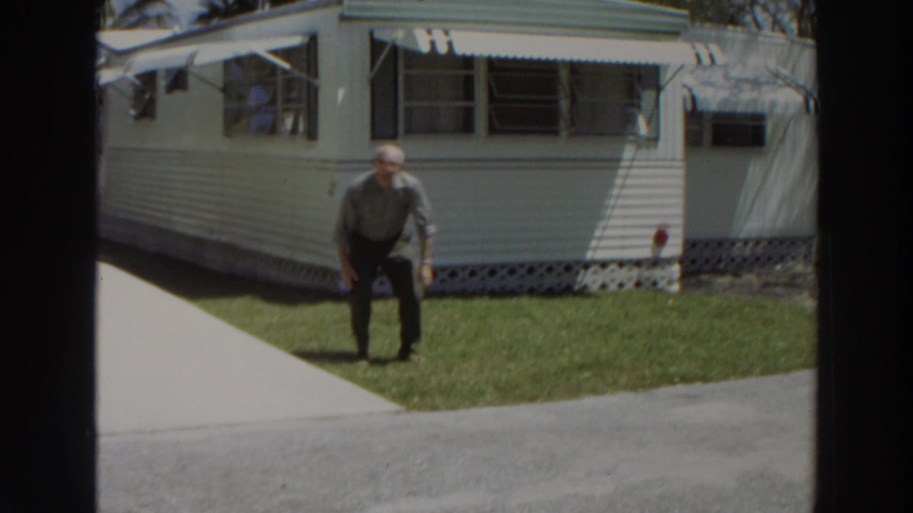 Man stands on a lawn in front of a white mobile home with awnings.