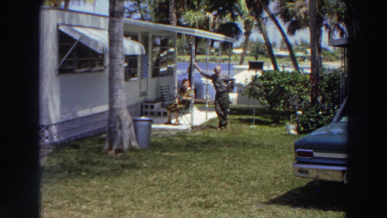 A man stands near a white trailer while a woman sits under the patio overhang.