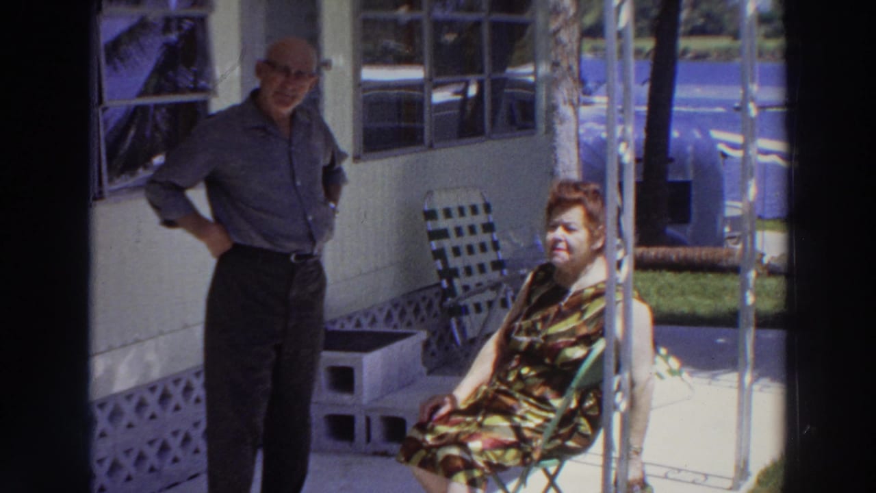 The couple appears on a porch in Puerto Rico, with the man standing and the woman seated near lawn furniture and a pool beyond.