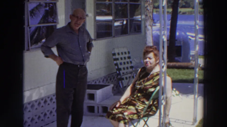 A closer 8mm view shows the man standing near the wall and the woman seated in patterned dress on the porch.