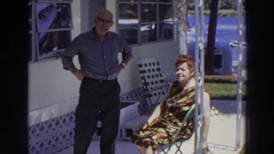 Late frame of the Puerto Rico home movie shows the woman seated in sunlight and the man standing beside the porch wall.