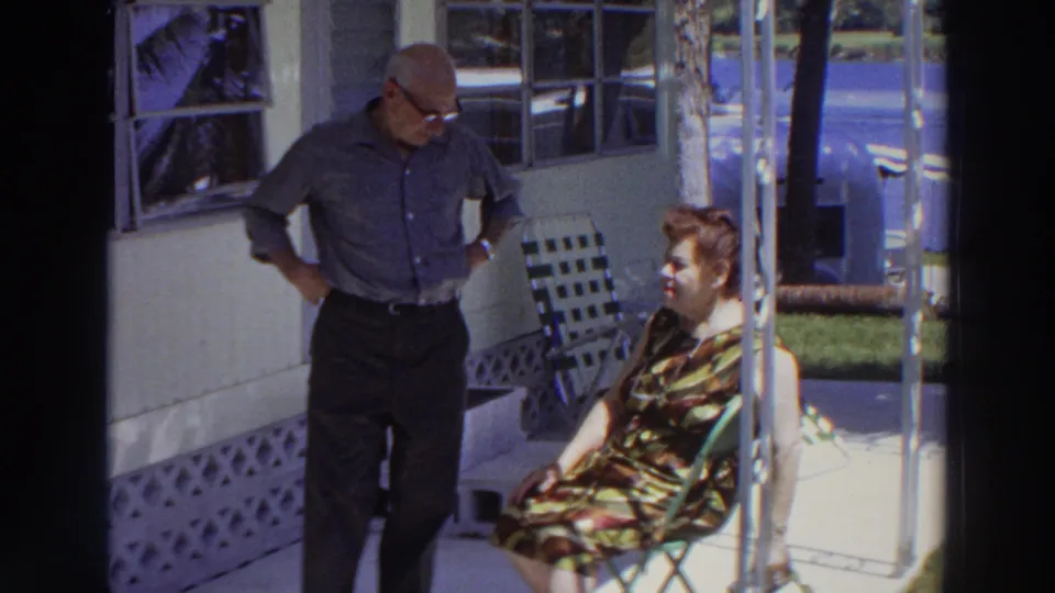 In 1966 Puerto Rico home-movie footage, an older man stands with hands at his waist while an older woman sits on a porch chair.