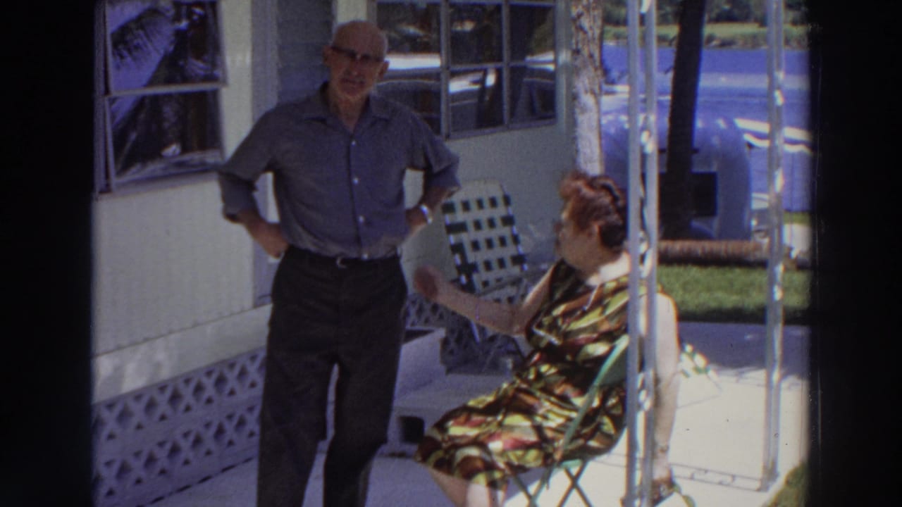 Seated woman gestures toward standing man on a porch.