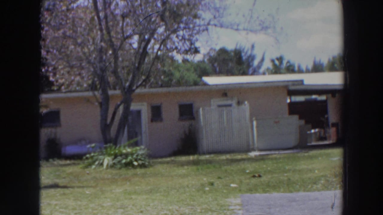 1966 Puerto Rico home-movie view of a low residential building, lawn, trees, and white doors seen past a dark door or window edge.