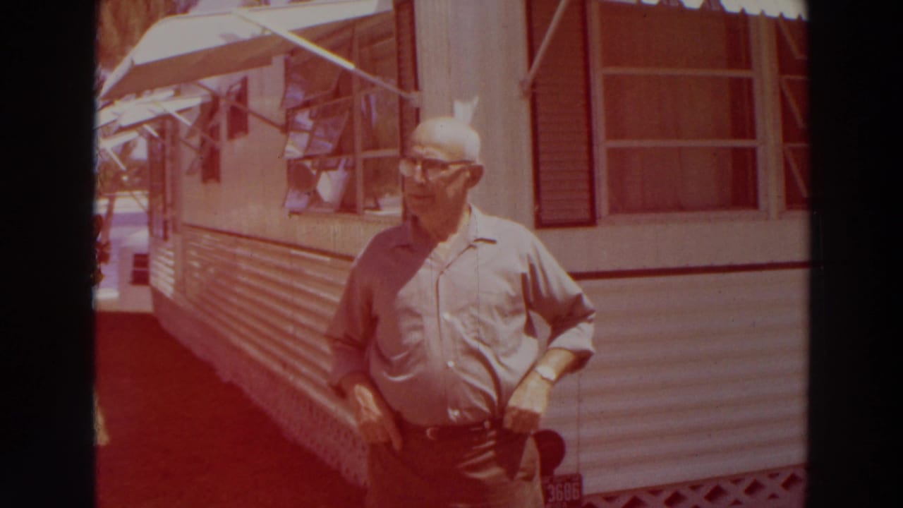 Older man in glasses and a light shirt stands beside a white mobile home in Puerto Rico, with awning windows and siding visible.