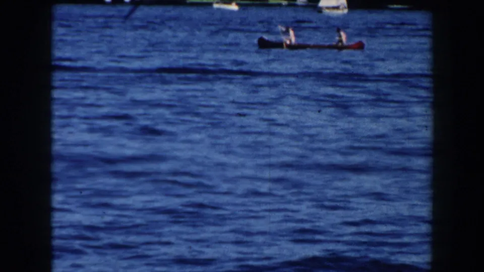A red canoe with two people crosses the lake in the distance during the 1960 Brighton, Michigan home-movie scene.