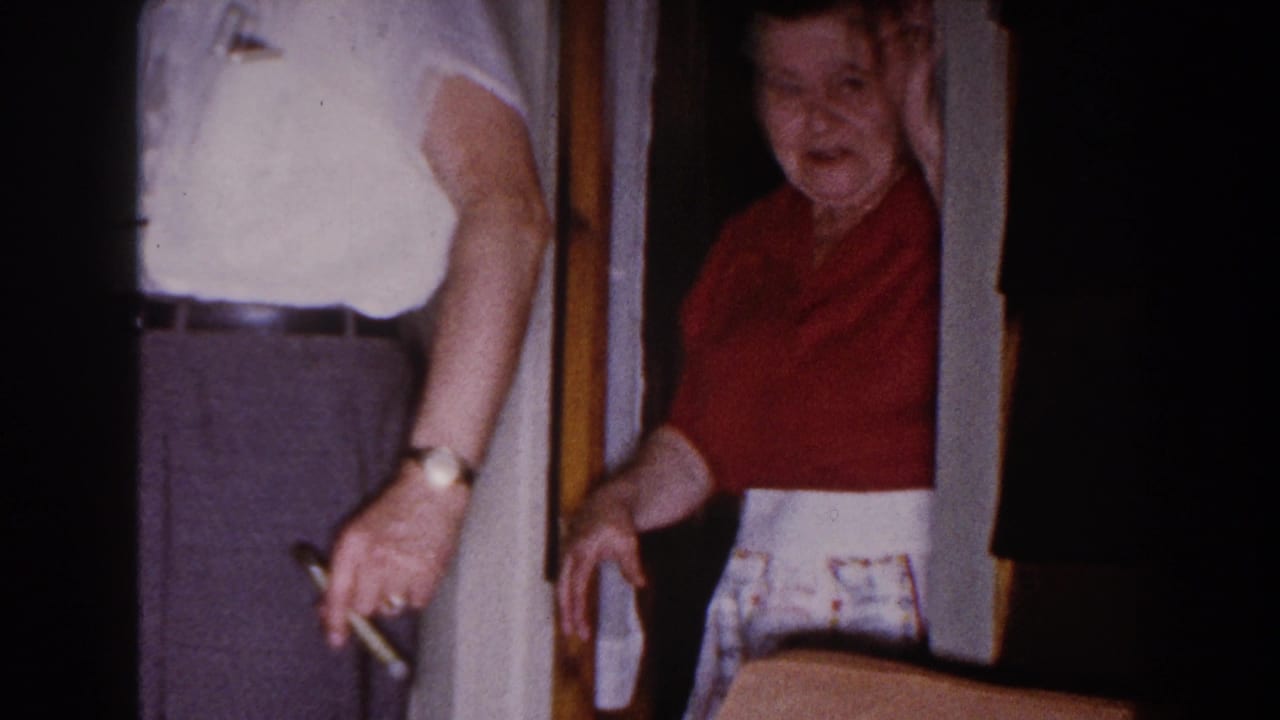 In a Brighton, Michigan home-movie frame from 1960, a woman in a red blouse stands at a doorway beside a man in a white shirt.