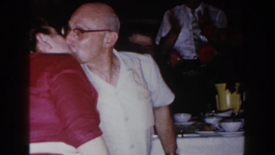 In 1960 Brighton, Michigan home-movie footage, an older man in glasses kisses a woman in a red dress at a family dinner table.