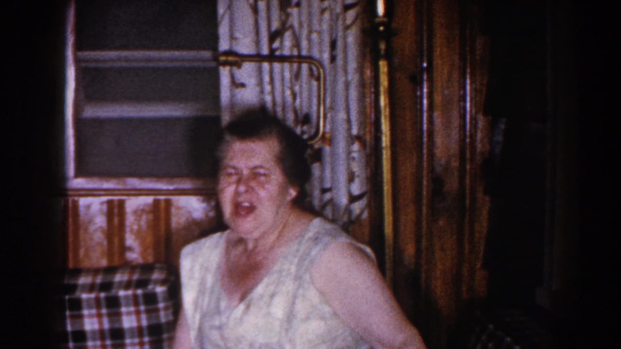 Woman facing the camera with mouth open in a dim interior room.