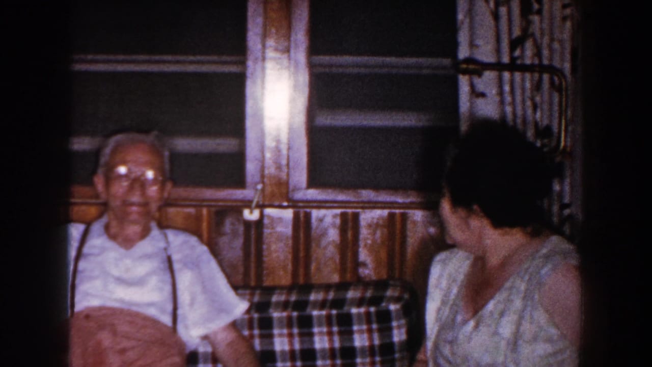Elderly man in glasses rests on a plaid couch while a woman sits beside him.