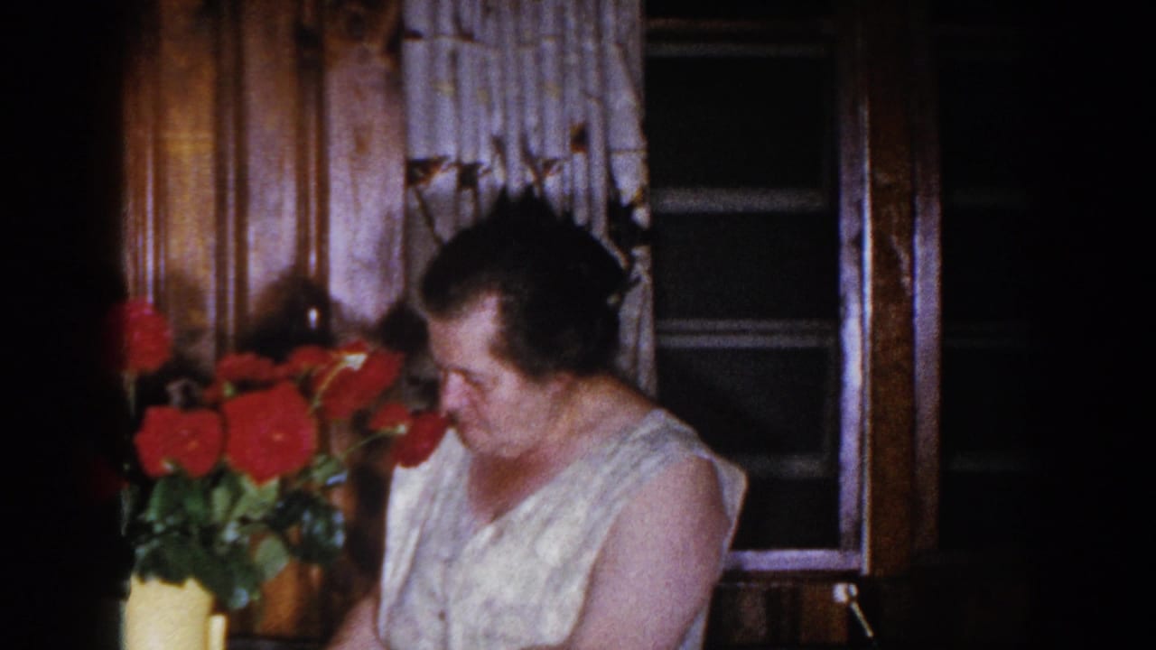 Woman looks down toward red roses in a yellow vase near a window.
