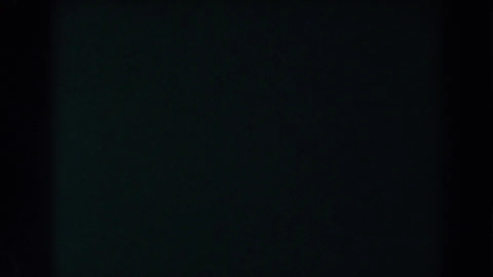 Low-light 8mm frame from the Brighton, Michigan reel, showing heavy darkness, grain, and a central vertical shadow area.