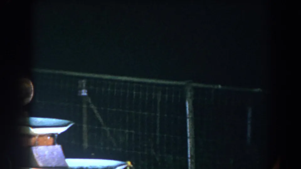 A dimly lit tiered fountain stands beside a chain-link fence in the Brighton backyard scene.