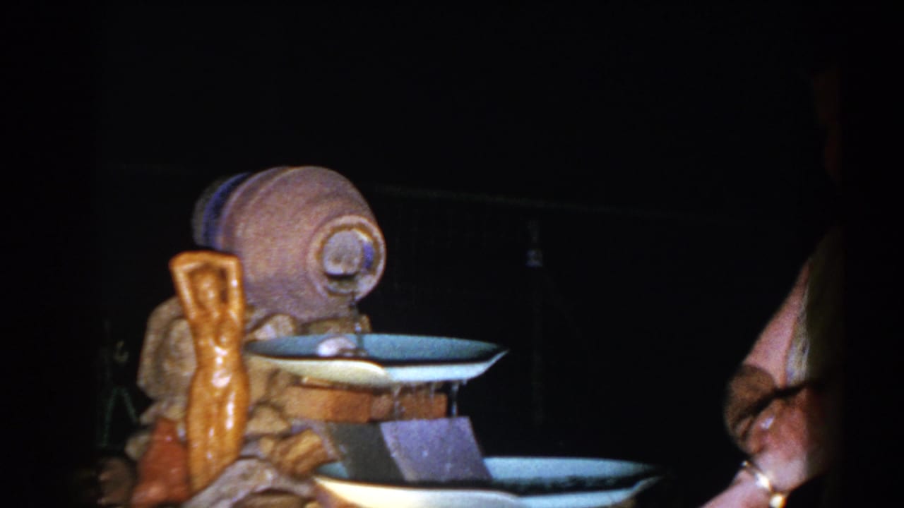 Tiered artificial fountain in a dark yard with a partial adult figure at the right edge.