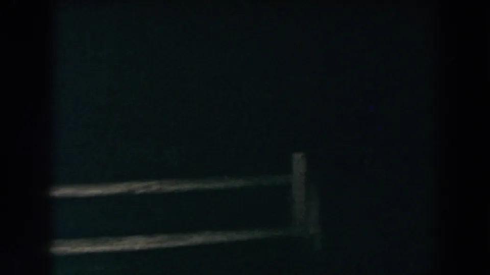 1960 Brighton, Michigan 8mm frame showing a shadowed yard, rough wooden fence rails, and the lower portion of a dark house exterior.
