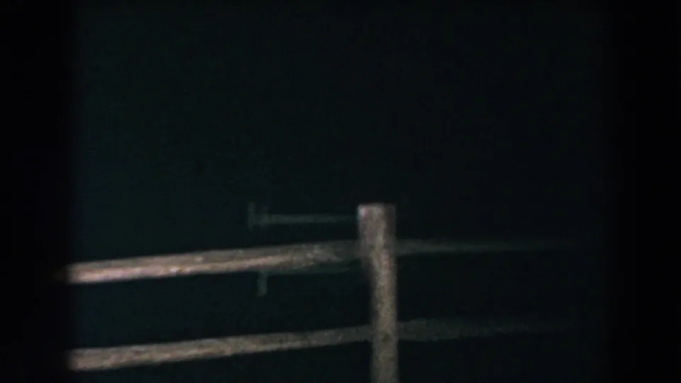 1960 Brighton, Michigan 8mm frame with a wooden fence foreground, dark rural house wall, small window, and exterior lights at night.
