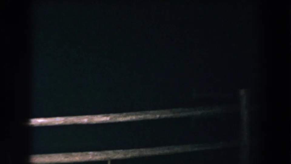 1960 Brighton, Michigan 8mm frame showing a dim wooden fence against a nearly black roadside background.