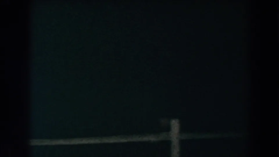 Underexposed 1960 8mm frame showing a low wooden rail and post at the bottom of a dark Brighton roadside scene.
