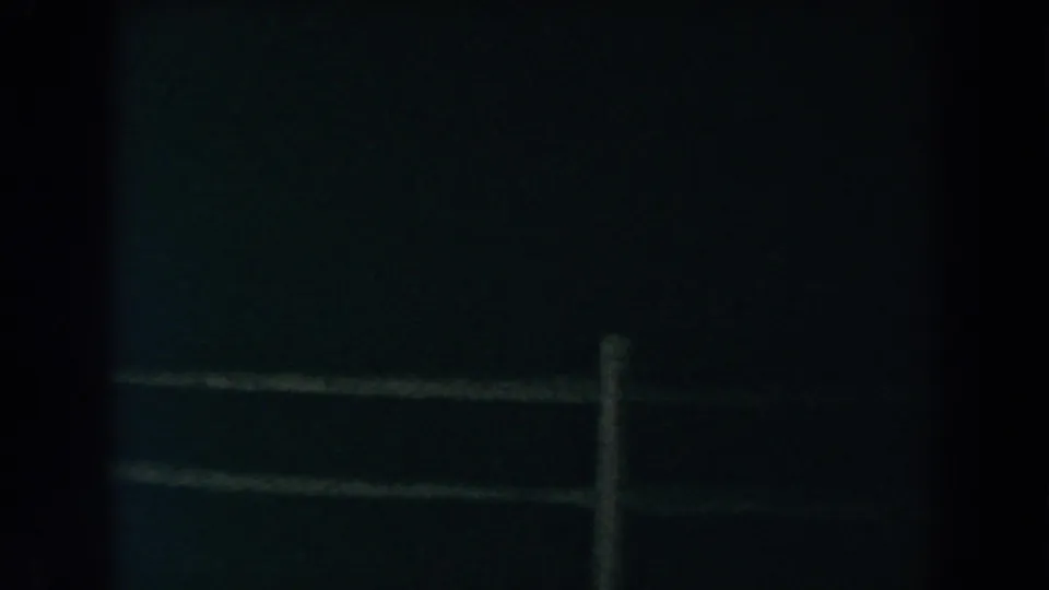 Grainy 8mm nighttime view of fence rails and a central post in Brighton, Michigan, with most surroundings obscured.