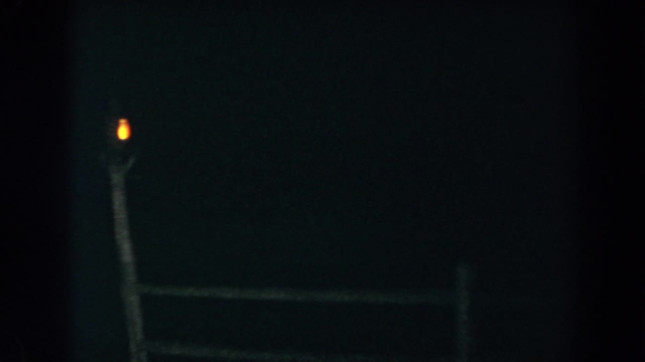 Dark exterior with a wooden fence and a small light glowing atop a post.