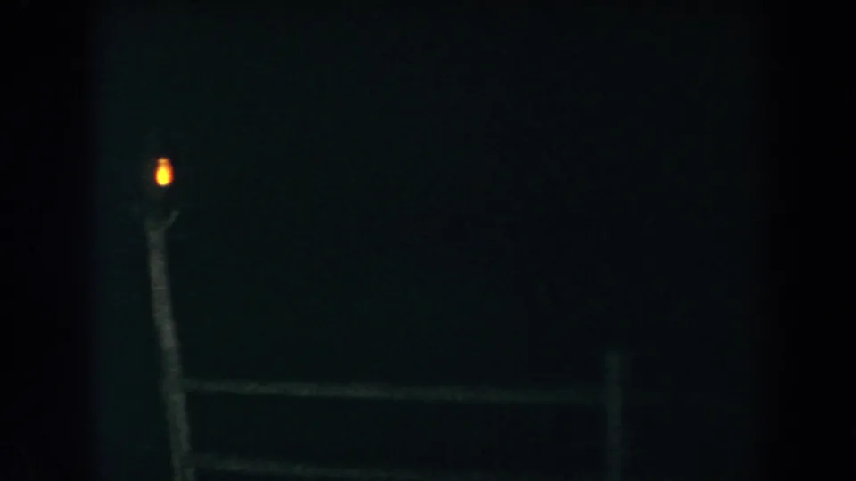 1960 Brighton, Michigan home-movie frame showing a dim wooden fence and a small post-top light in darkness.