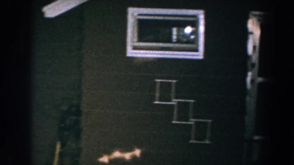 1960 Brighton, Michigan frame showing a small white-trimmed window with a visible light inside and white-outlined steps against a dark brown house exterior.