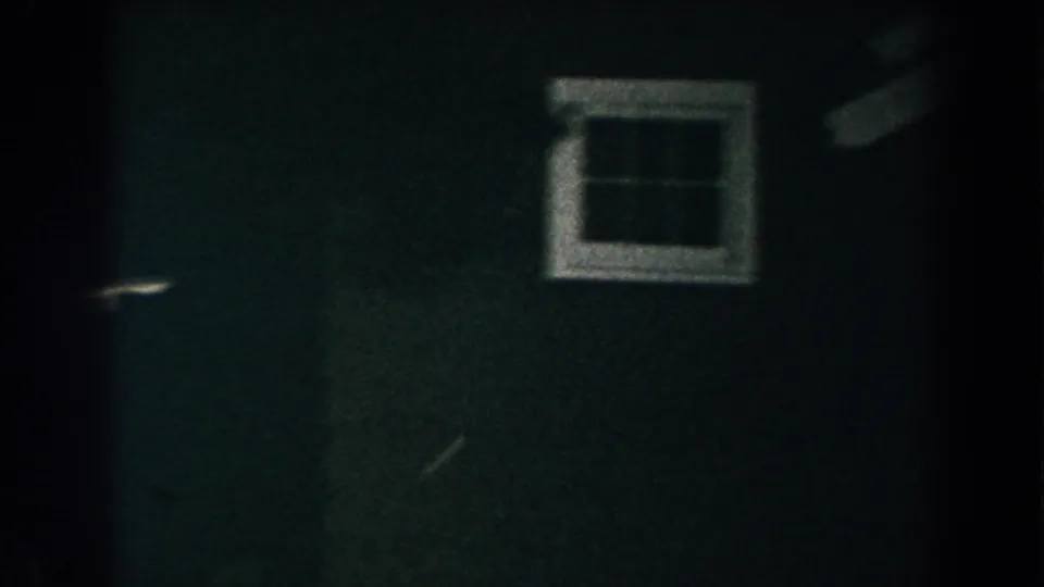 1960 Brighton, Michigan home-movie frame of a dark green house facade with a white-trimmed window at night.