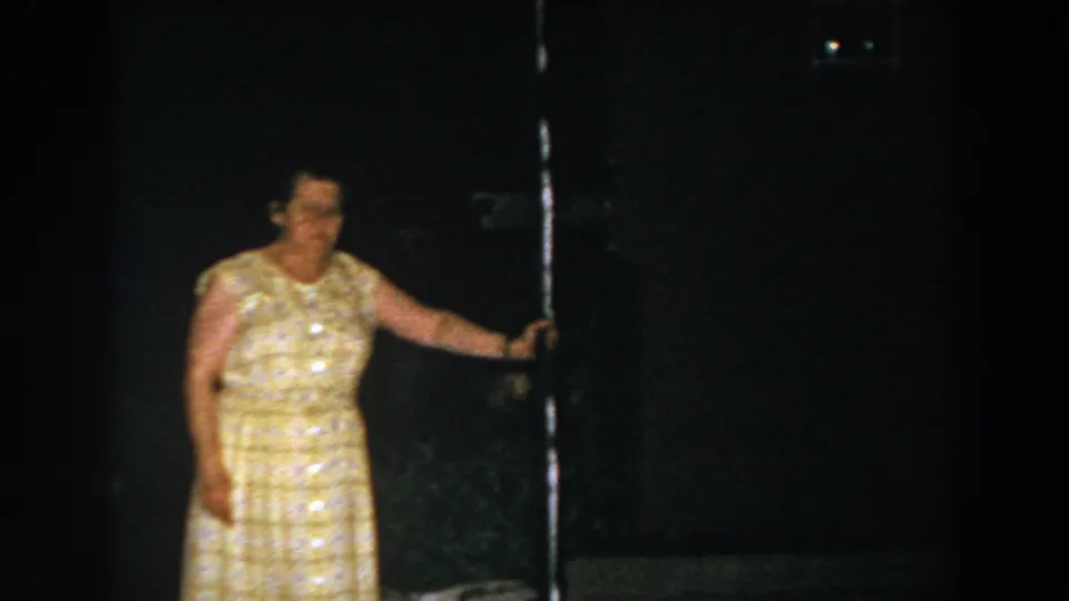 1960 Brighton, Michigan 8mm frame showing an adult woman near a dark doorway beside the house exterior.