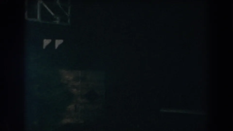 1960 Brighton, Michigan 8mm frame showing a nearly black exterior wall with faint window-like forms and a small reflected highlight.