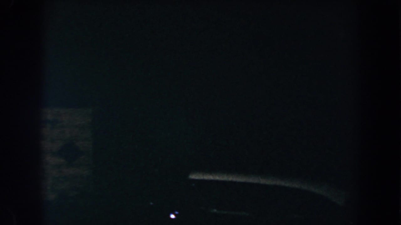 1960 Brighton, Michigan 8mm frame showing a barely visible car-like silhouette in deep nighttime shadow.