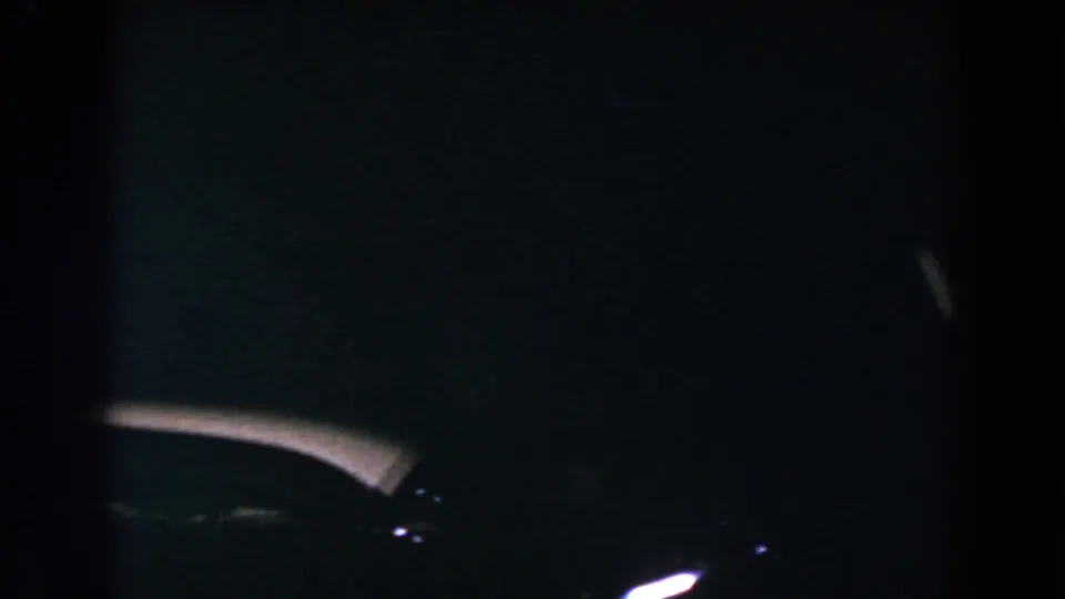 Low-light 1960 Brighton, Michigan frame with a pale curved highlight suggesting the top or hood of a vehicle.