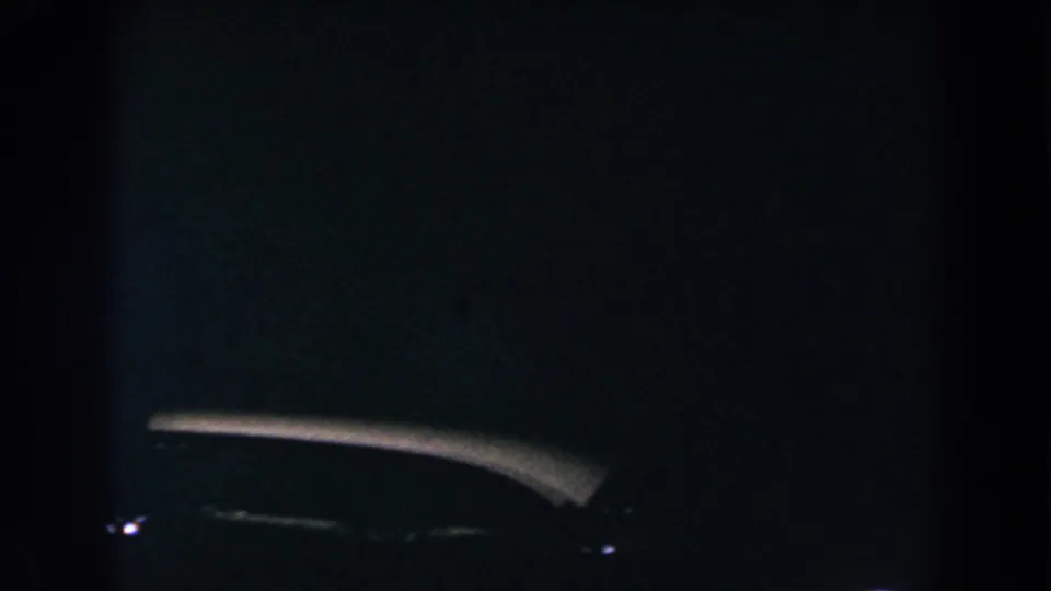 Grainy 8mm night frame from Brighton, Michigan, with a dark car-like silhouette and a faint bright edge.