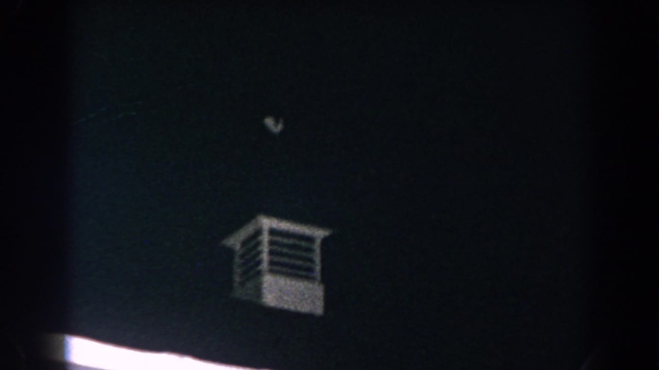 1960 Brighton, Michigan 8mm frame with a small white louvered tower over a mostly dark roofline and sky.