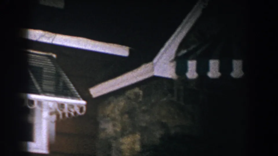 1960 Brighton, Michigan 8mm frame showing a brown and white roof structure, weather vane, and dark storm sky.