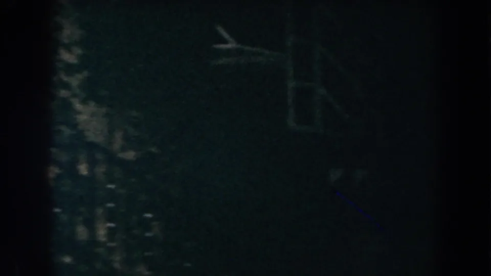 Dark 8mm frame from the Brighton exterior sequence, with shadowed foliage or siding and a faint rectangular feature near the upper right.