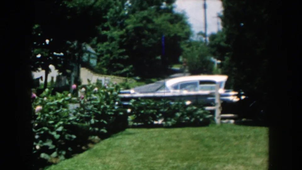 The period sedan continues past the suburban lawn and rose bushes in Brighton, Michigan, filmed on 8mm in 1960.