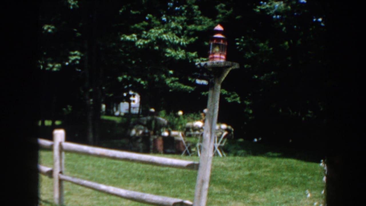 Backyard lawn with fence rail, lantern post, trees, and garden furniture near the rear.