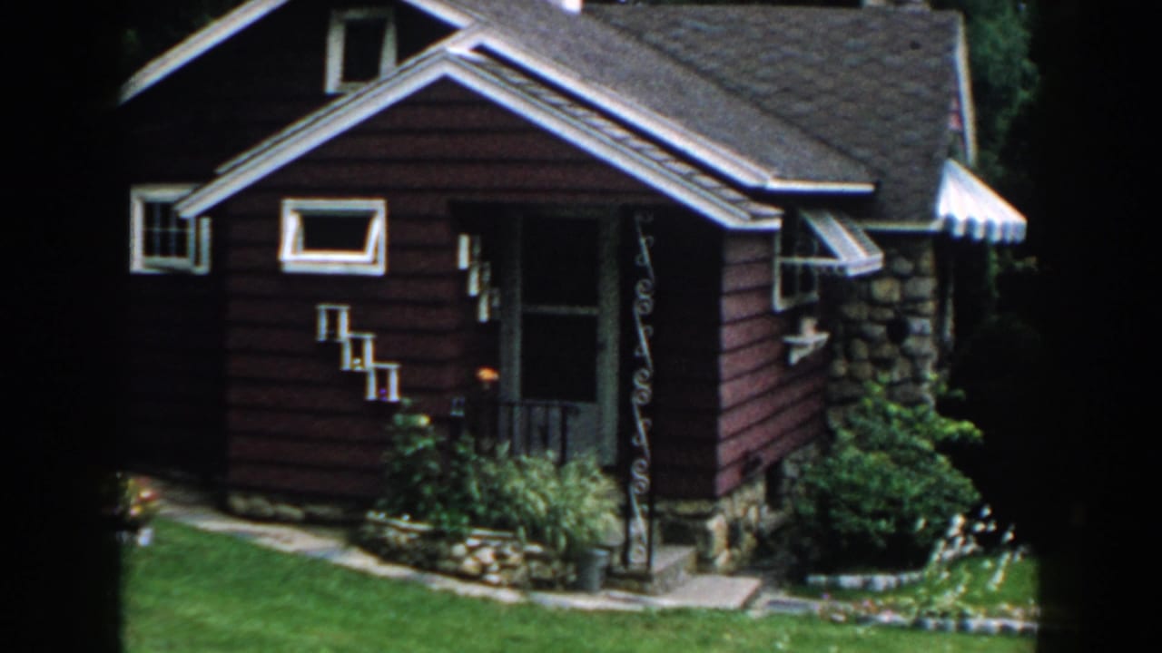 Red bungalow with white trim, stone foundation, porch awning, shrubs, and front lawn.