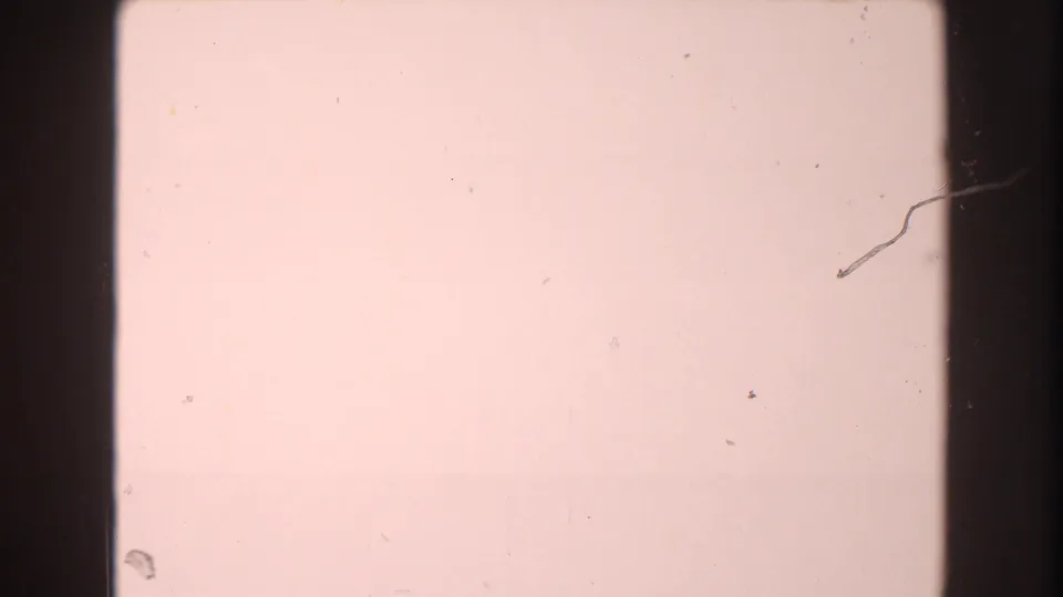 Near-blank overexposed 8mm frame from the 1960 Brighton, Michigan clip, showing gate shadows, dust specks, and a thin scratch mark.
