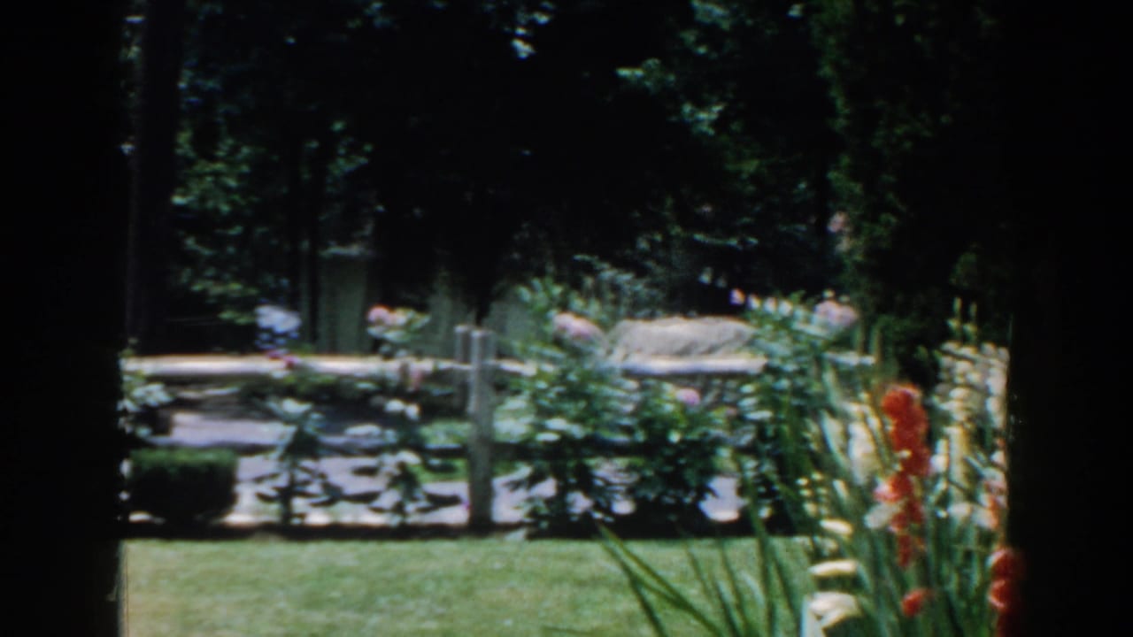 Green lawn, white fence, flower beds, and trees around a shaded garden.