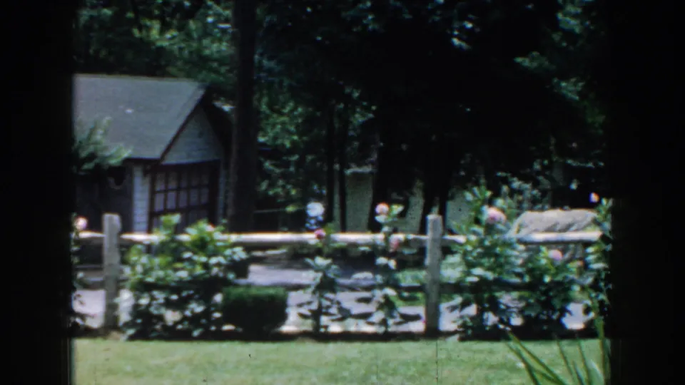 A small house appears beyond the fenced garden in this 1960 Brighton, Michigan residential yard scene.