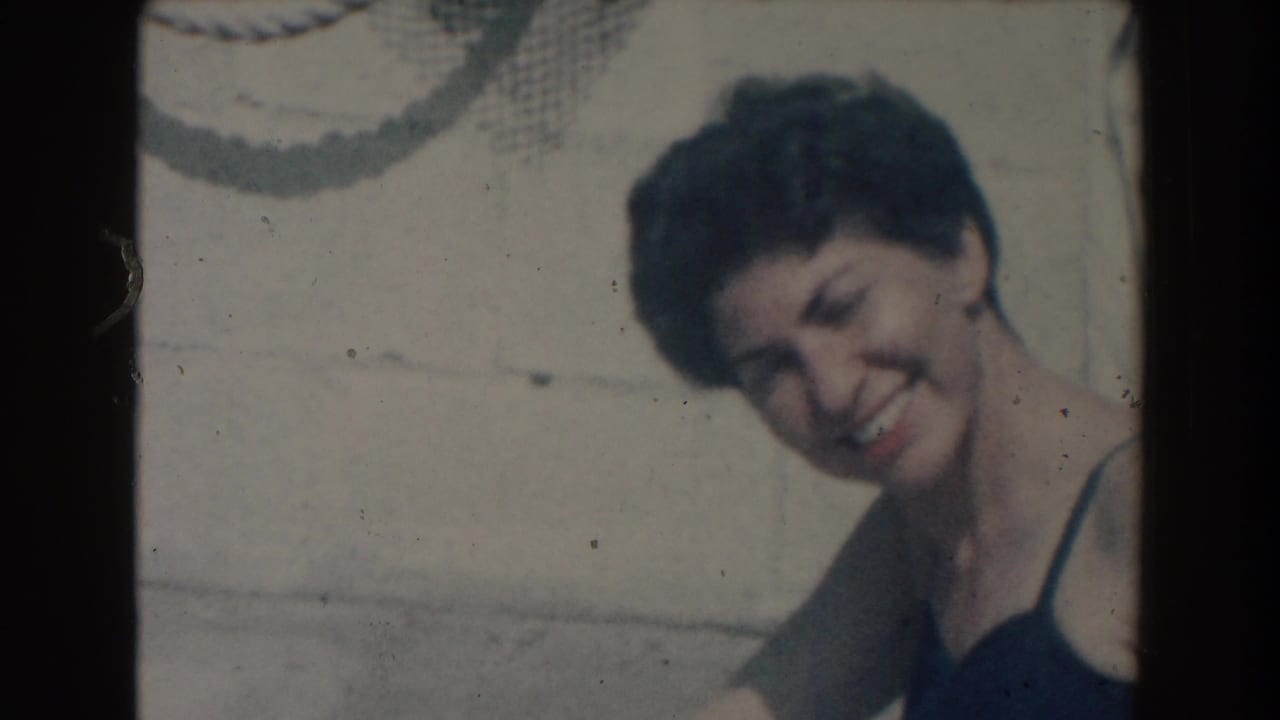 Woman in a dark swimsuit smiling beside a pool with a rope and wall behind her.
