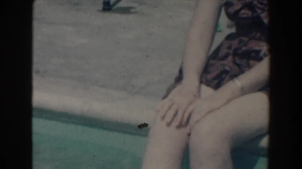 A seated adult in patterned clothing is cropped at the poolside, with hands, legs, and turquoise pool water visible.