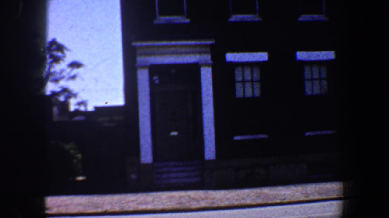 Dark brick three-story residence with white trim, doorway, windows, steps, and bright sky at the left edge.